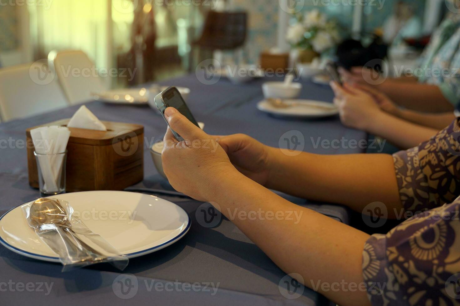 Customers are surfing the internet on their mobile phones while waiting for dinner to be ordered at the table. soft and selective focus. photo