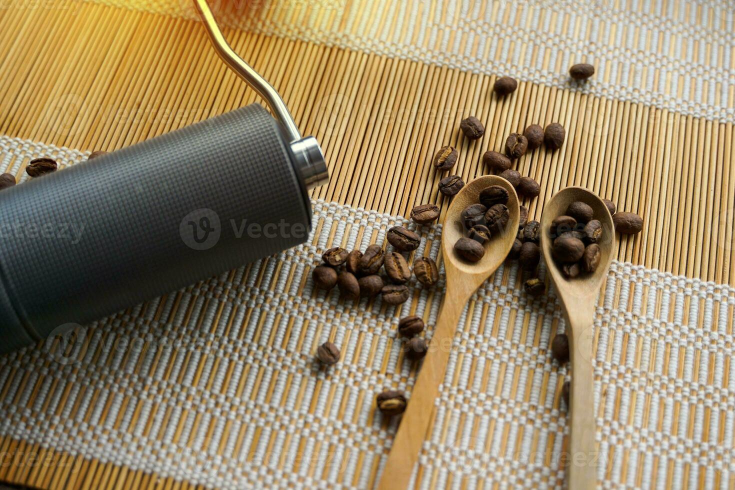 Grinder and coffee beans in a wooden spoon on bamboo mat background for a simple black coffee drip by yourself and people who like special aromas and flavors specific to that coffee bean. photo