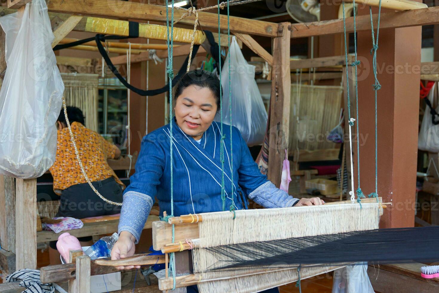 Asian female weavers weaving traditional patterns with hand weaving machines.in the concept of OTOP, community products, hand weaving fabrics, community shops, community weaving centers. photo