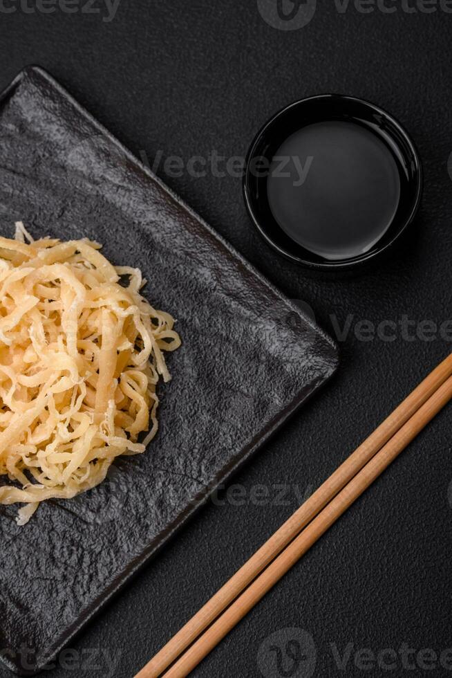 Delicious dried squid in the form of shavings with salt and spices on a ceramic plate photo