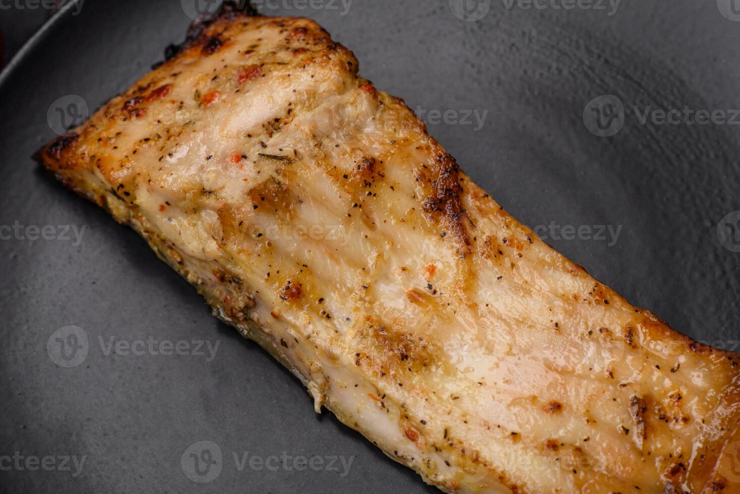 Slice of delicious baked fish with salt, spices and herbs on a ceramic plate photo