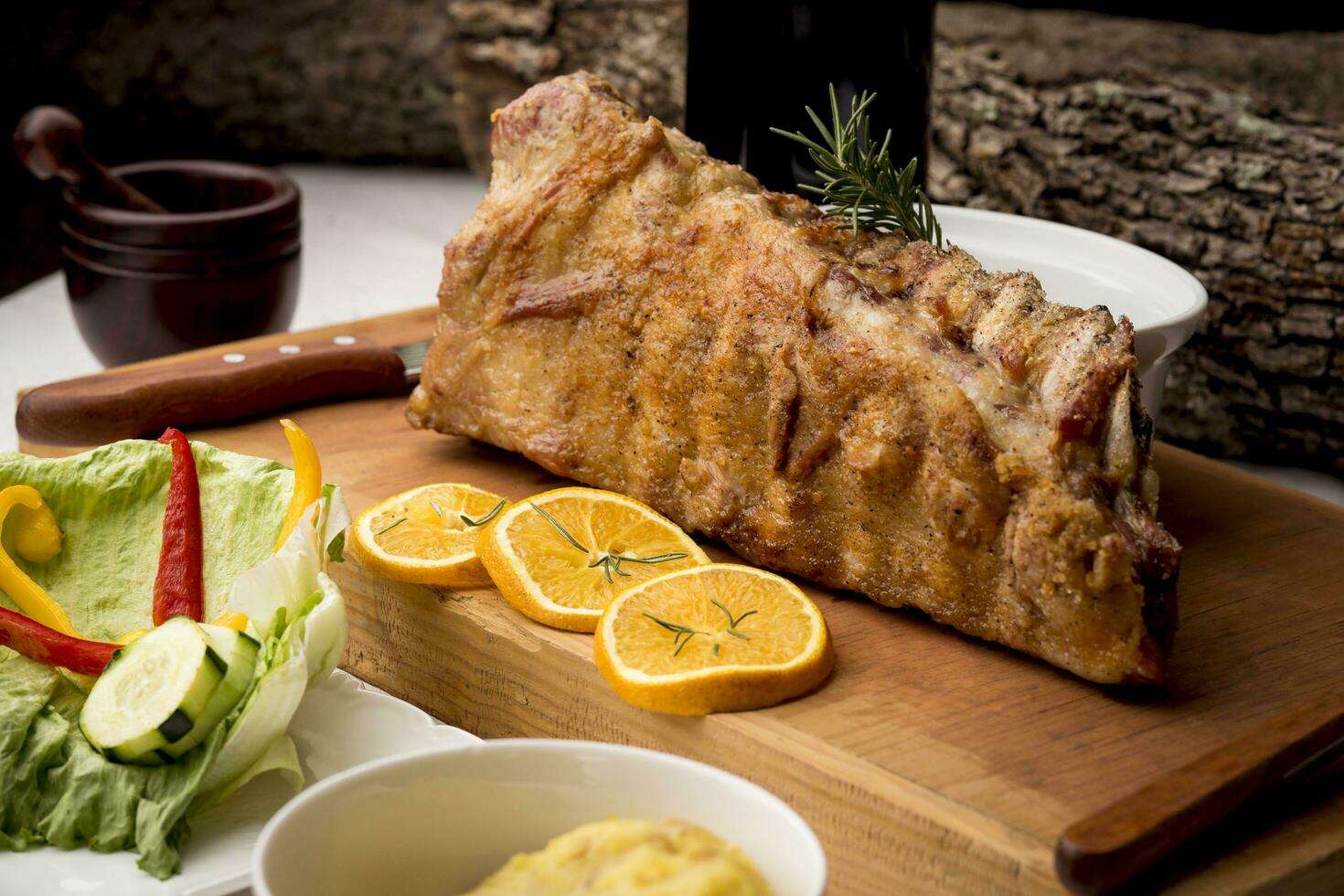 Smoked pork ribs and rosemary herbs on wooden board - salad, mashed potatoes and oranges slices photo