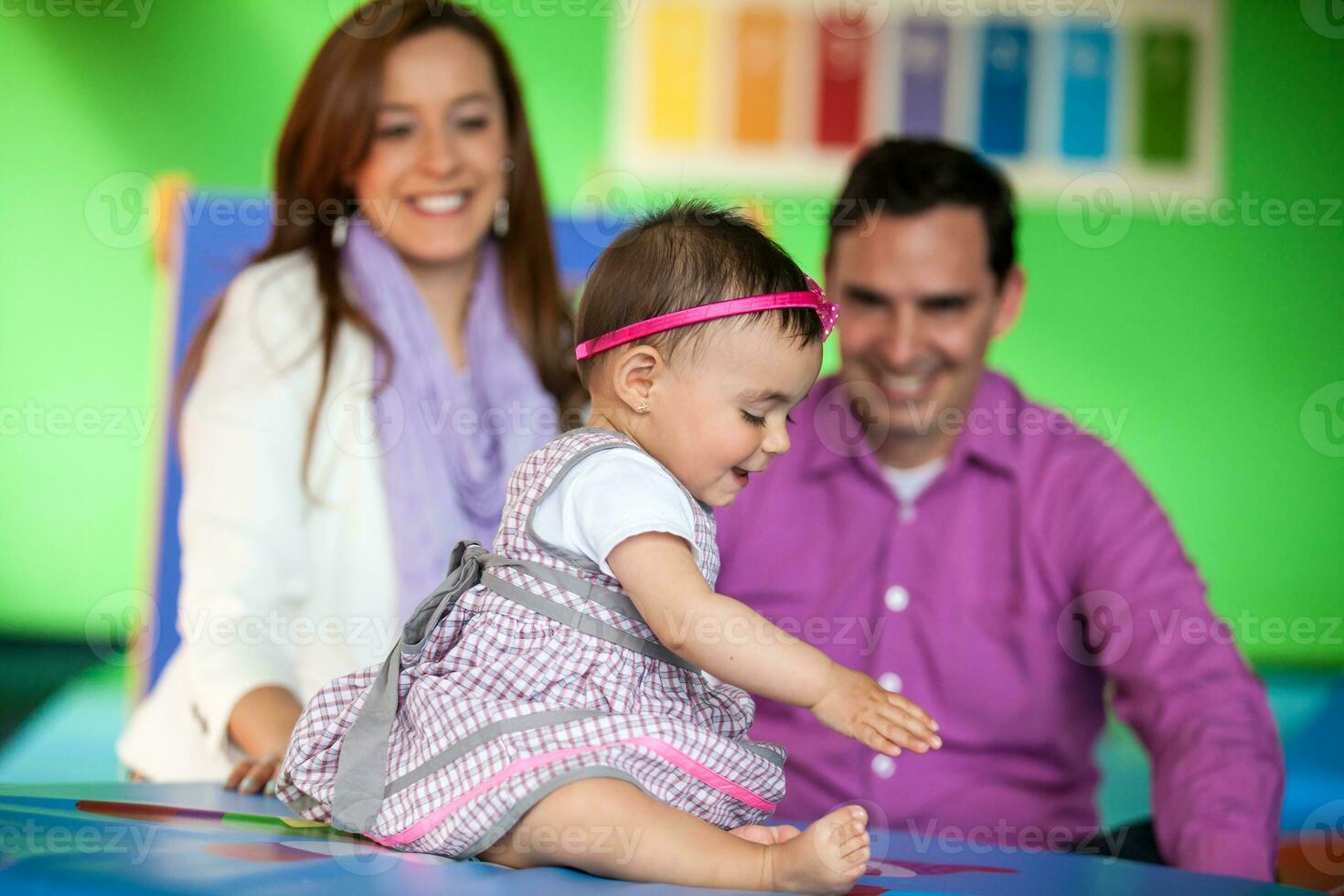 Beautiful ten months baby girl playing with her parents on background. Early stimulation for toddlers concept. photo