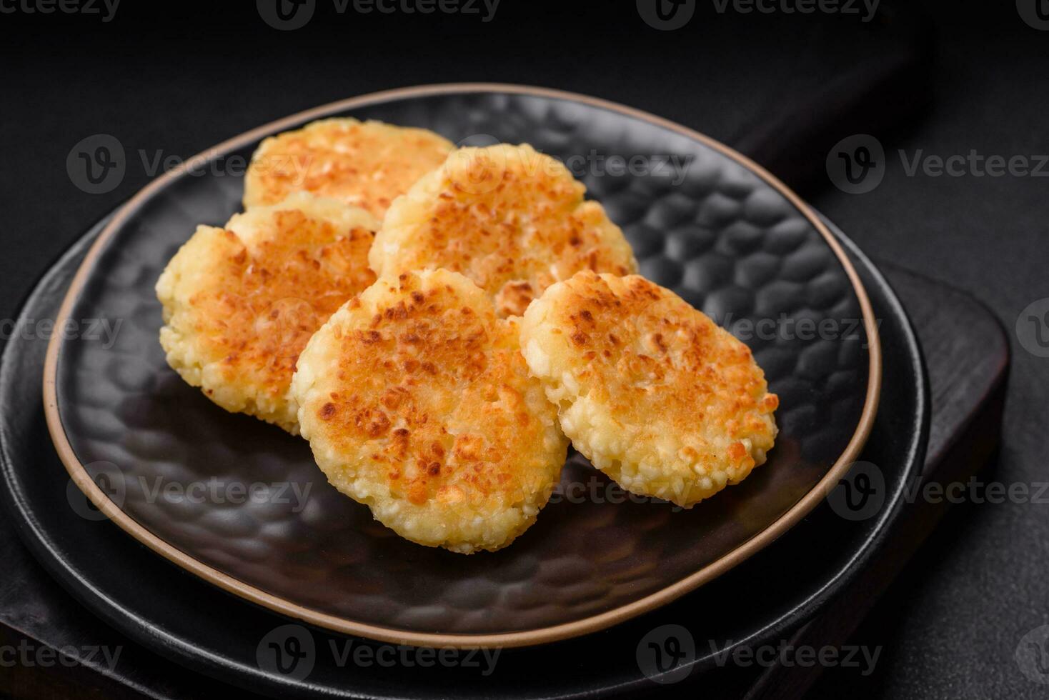 Delicious fresh cottage cheesecakes with raisins and vanilla on a black ceramic plate photo