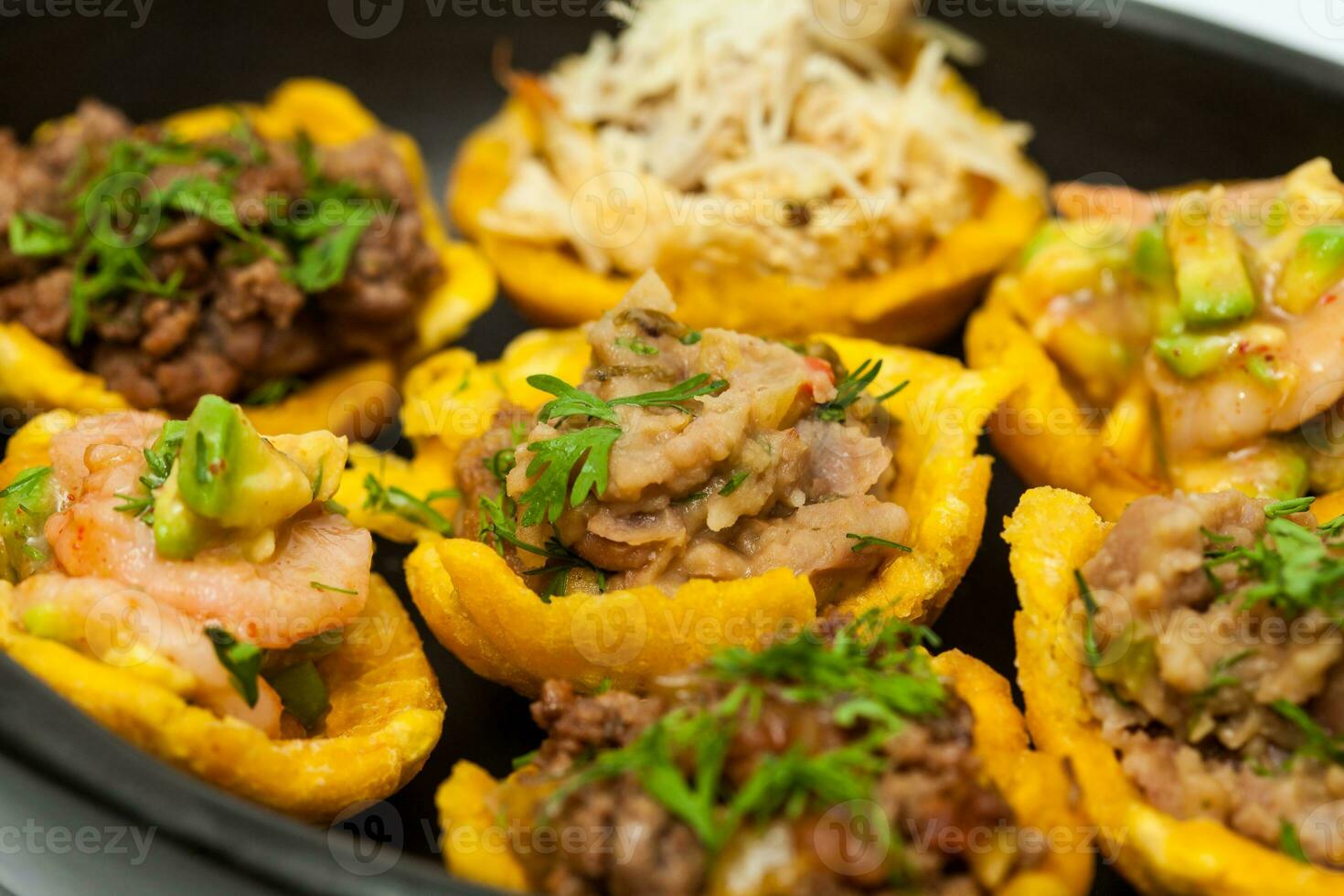 Plantain cups filled with different types of stuffing on black ceramic dish photo