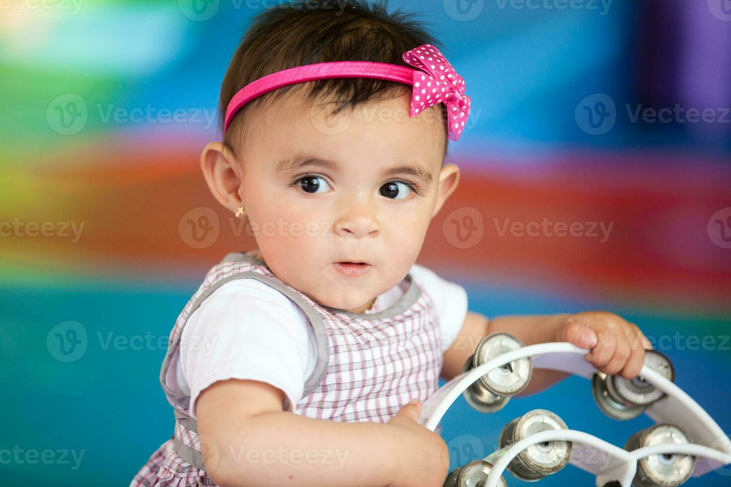 Beautiful ten months baby girl playing with a tambourine. Early stimulation for toddlers concept. photo