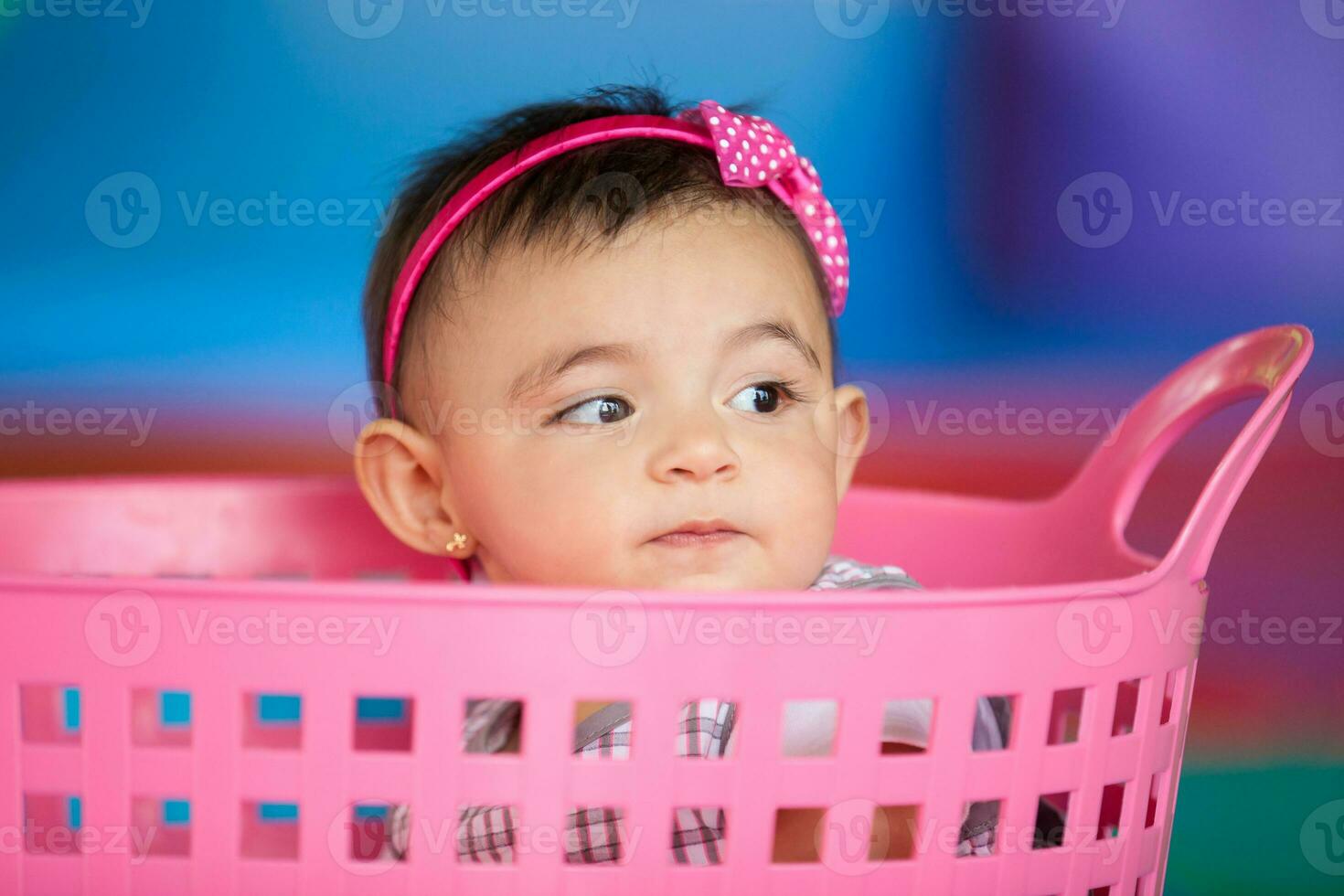 Beautiful ten months baby girl playing in a pink basket. Early stimulation for toddlers concept. photo