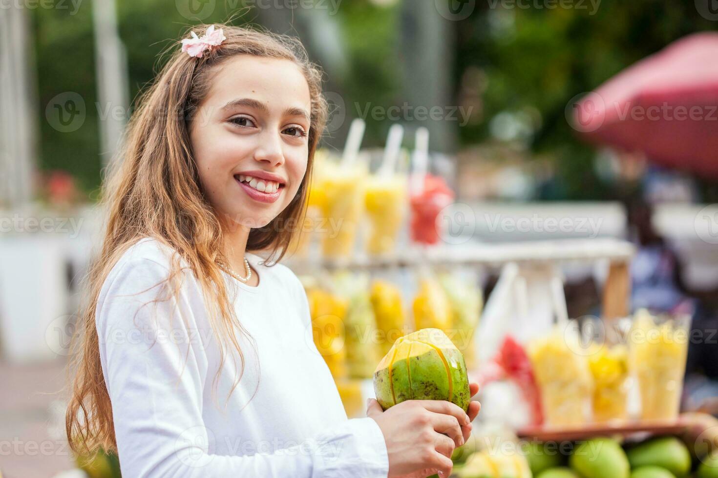 hermosa joven niña a paseo bolívar cuadrado en el ciudad de cali comiendo tropical frutas en Colombia foto