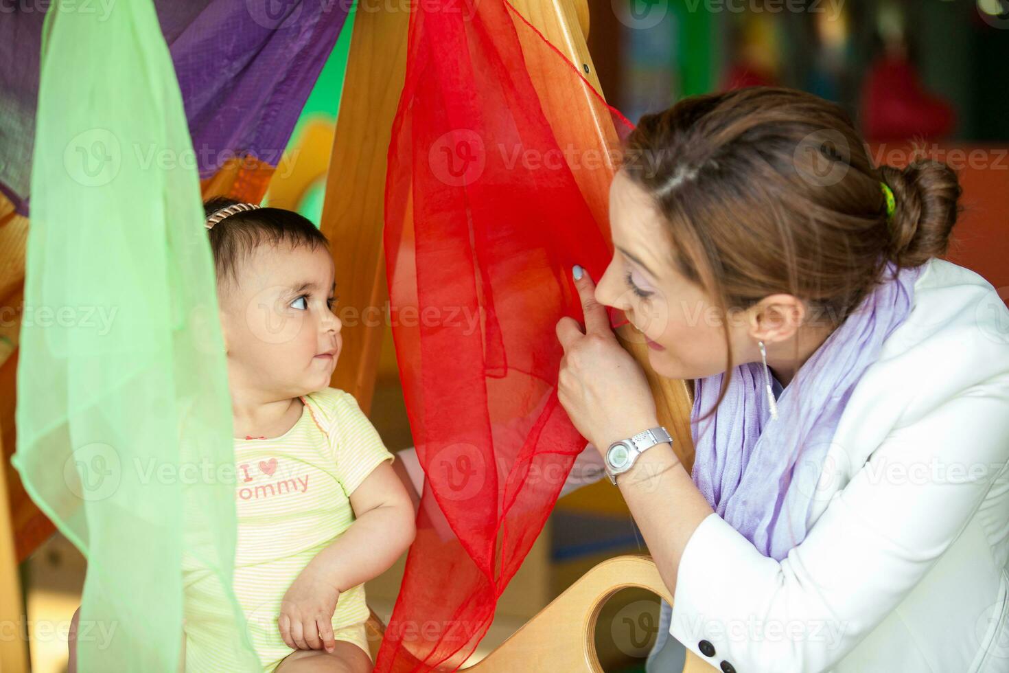 hermosa diez meses bebé niña jugando con vistoso telas y su mamá. temprano estímulo para niños pequeños concepto. foto