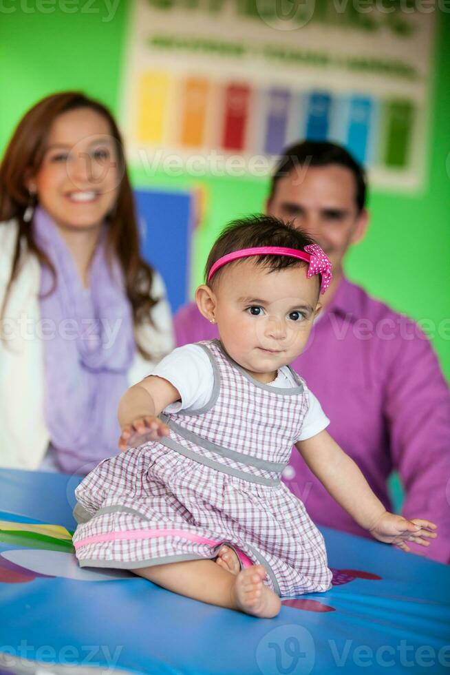 Beautiful ten months baby girl playing with her parents on background. Early stimulation for toddlers concept. photo