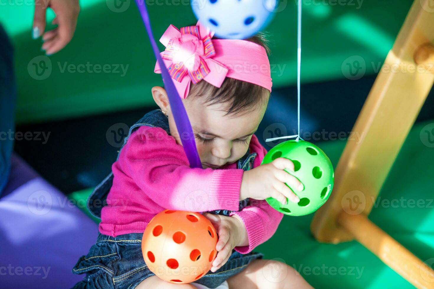 Beautiful ten months baby girl playing with colorful balls. Early stimulation for toddlers concept. photo