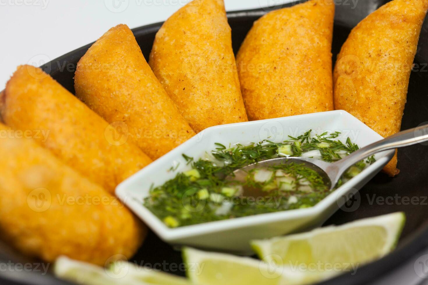 Typical Colombian empanadas served with spicy sauce on traditional black ceramic dish photo
