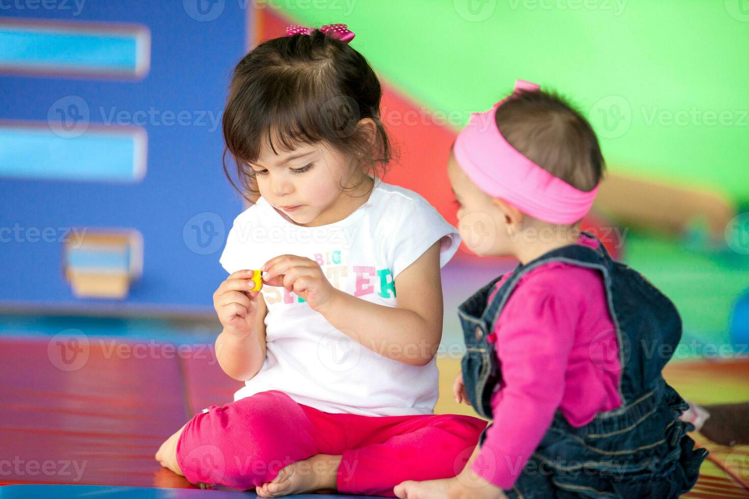 Beautiful small girl playing with her ten months baby girl sister. Early stimulation for toddlers and children concept. photo