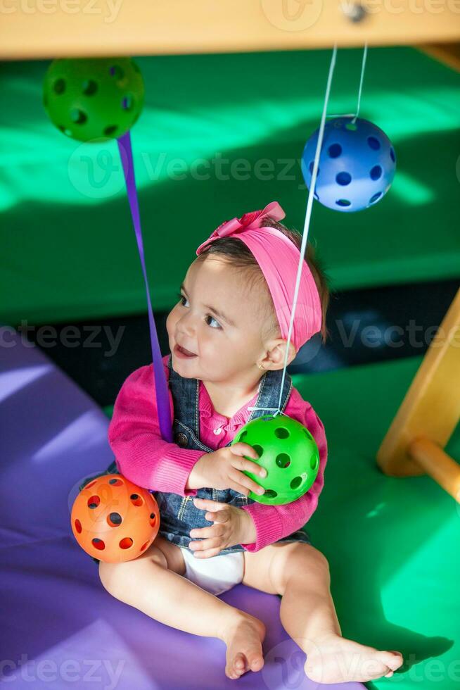 Beautiful ten months baby girl playing with colorful balls. Early stimulation for toddlers concept. photo