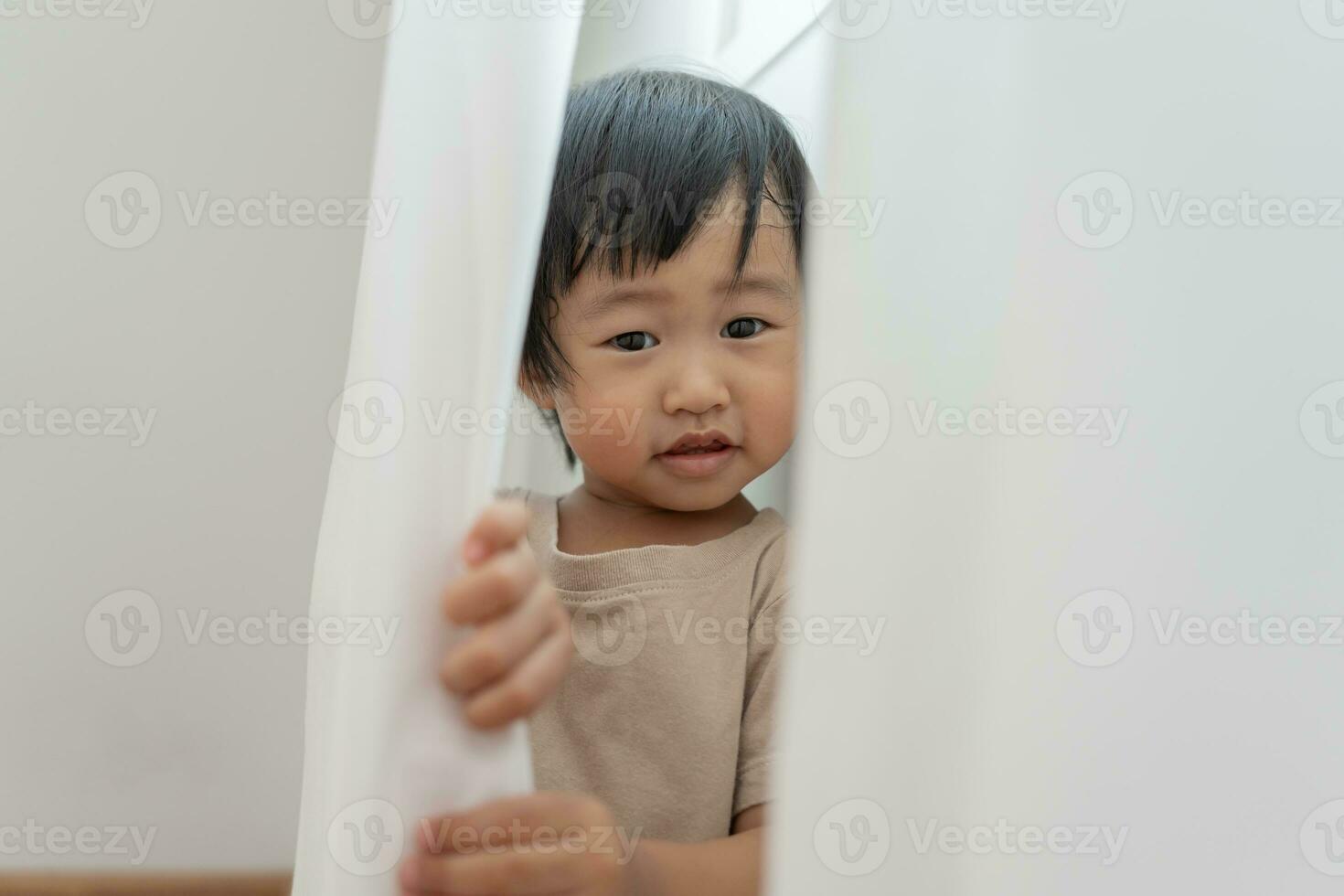 pequeño asiático niños niño , jugando esconder y buscar en pie siguiente un pared casa, adorable niño teniendo divertido en el hogar. contento familia tener divertido con niños, actividad, aprendizaje foto