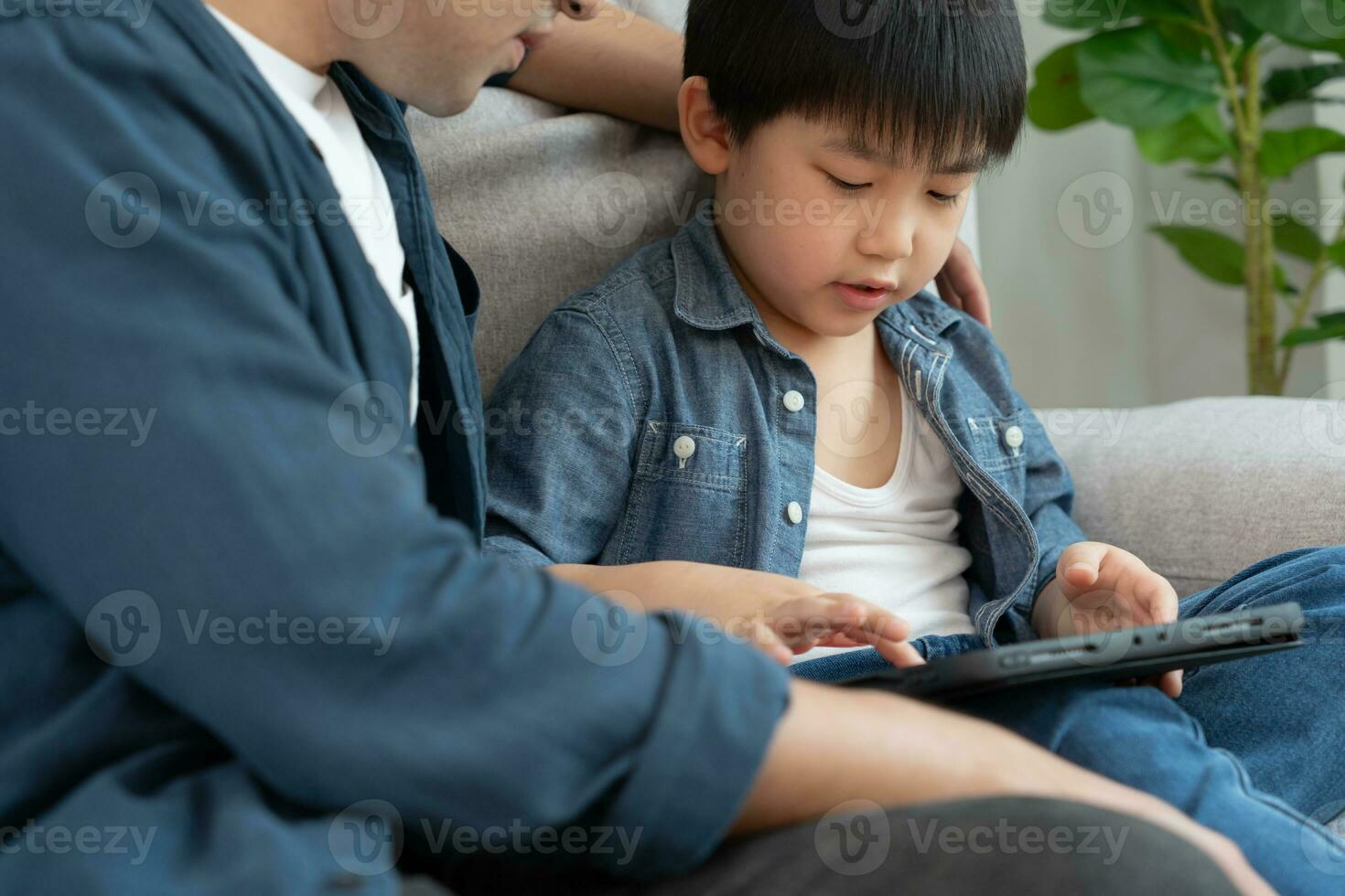 Happy single father playing teach using tablet with the little boy. family is happy and excited in the house. Father and son having spending time together, Good daddy , addiction fix, handle, control photo
