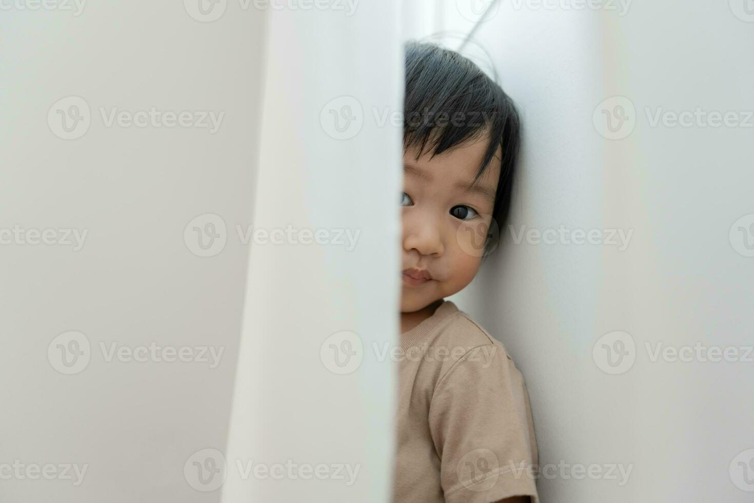 pequeño asiático niños niño , jugando esconder y buscar en pie siguiente un pared casa, adorable niño teniendo divertido en el hogar. contento familia tener divertido con niños, actividad, aprendizaje foto