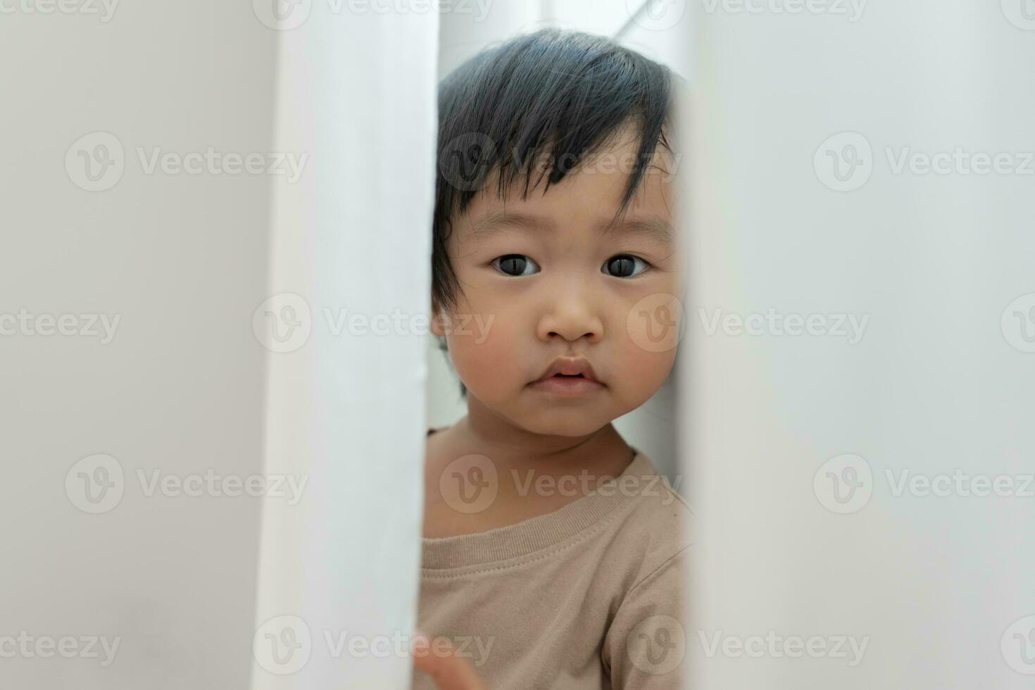 pequeño asiático niños niño , jugando esconder y buscar en pie siguiente un pared casa, adorable niño teniendo divertido en el hogar. contento familia tener divertido con niños, actividad, aprendizaje foto