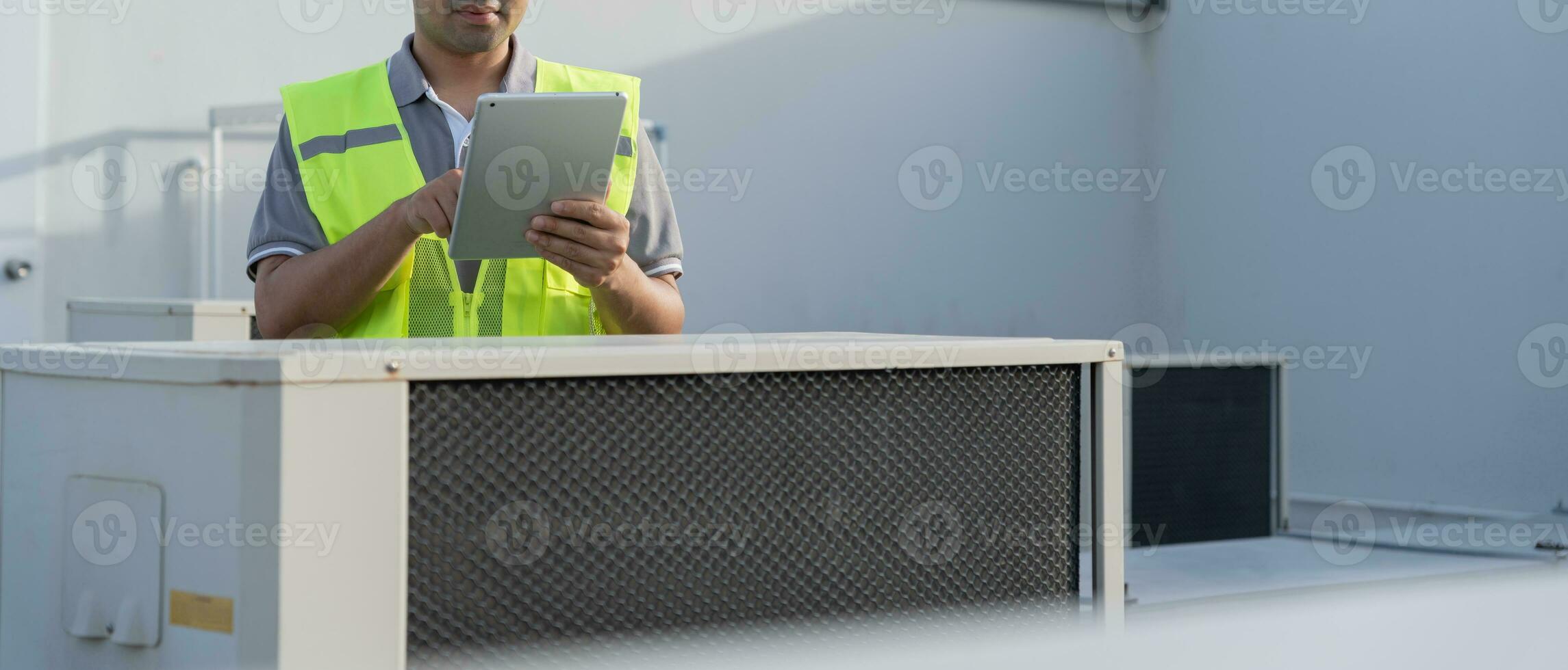 Asian maintenance engineer works on the roof of factory. contractor inspect compressor system and plans installation of air condition systems in construction. technology, online, mobile application. photo
