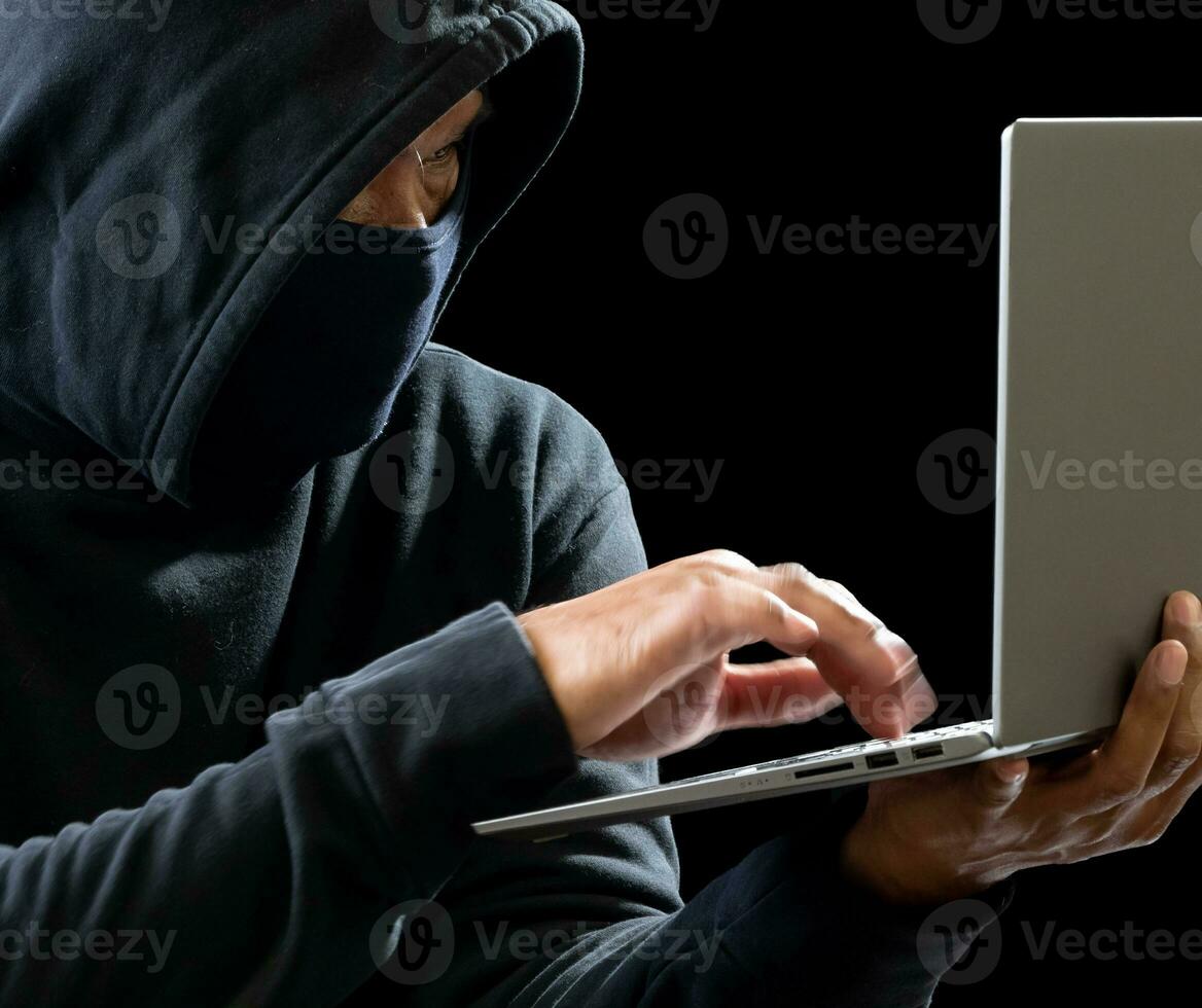 Hacker spy man one person in black hoodie sitting on a table looking computer laptop used login password attack security to circulate data digital in internet network system, night dark background. photo