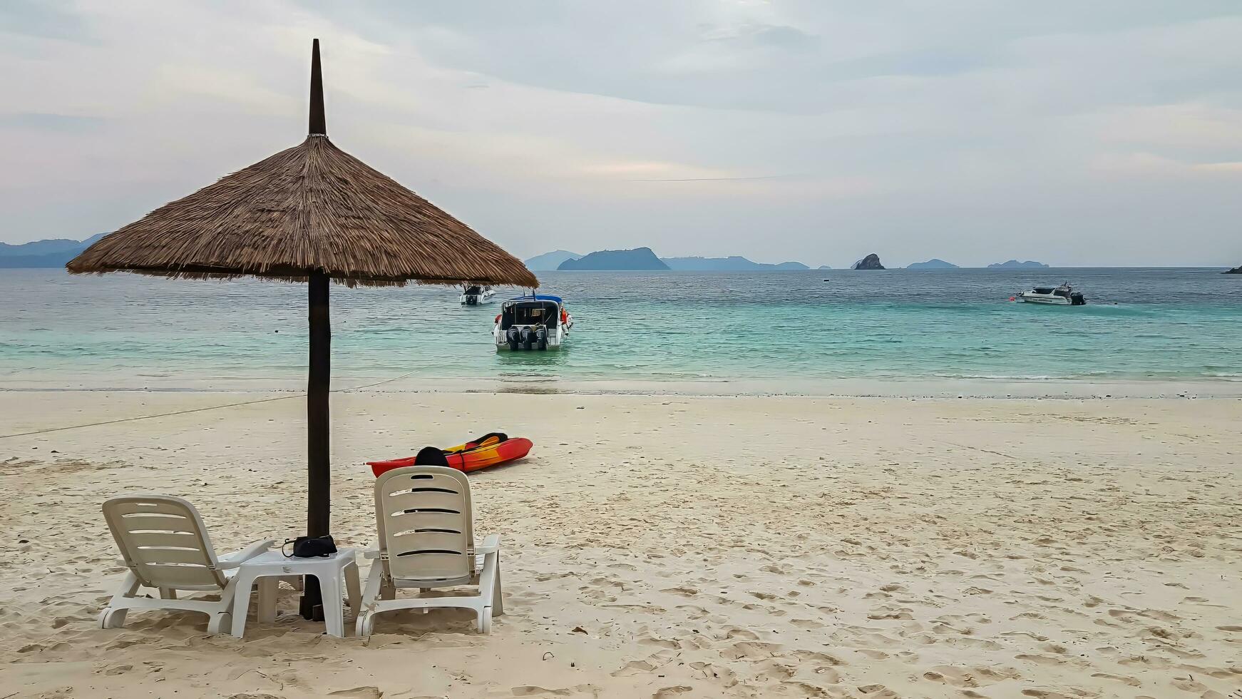 Beach chairs, umbrellas, kayaks on the beach, looking out over the sea, overlooking the island and speed boats or yacht Uncrowded people on an island in Myanmar photo