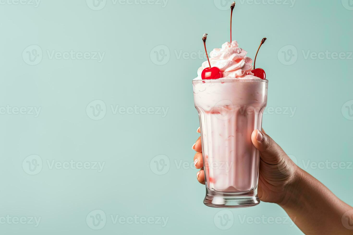 Female hand holding pink milkshake with cherry on blue background. photo