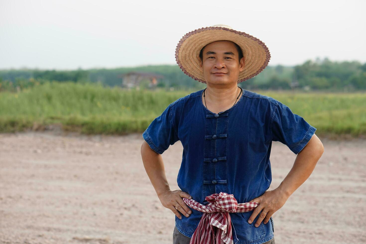 Handsome Asian man farmer wears hat, blue shirt, put hand on waist. feel confident.  Concept , Agriculture occupation. Thai Farmer . photo