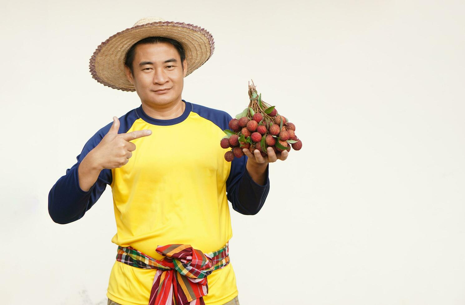 Handsome Asian man farmer wears hat, yellow shirt, holds litchi fruits. Concept, agriculture occupation.  Thai farmers grow organic litchis as an export product of Thailand. photo