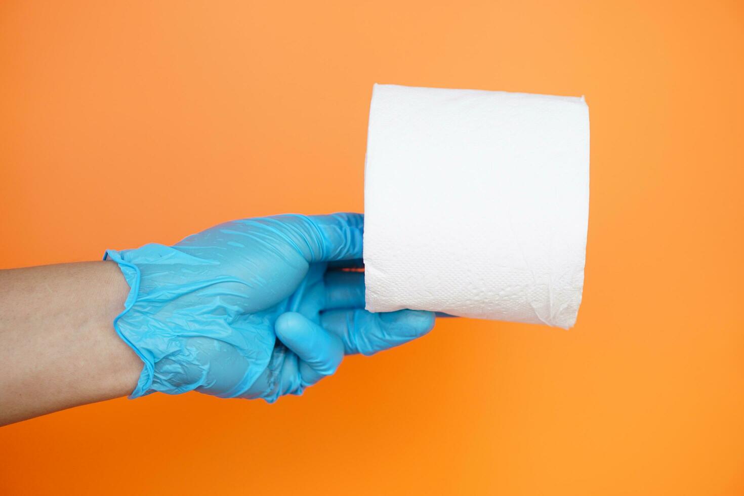 Close up hand holds roll of white tissue paper, isolated on orange background. Concept, cleaning tool, hygienic to wipe dirty and absorb wet ,use tissue paper for hygienic and sanitary.Toilet paper photo