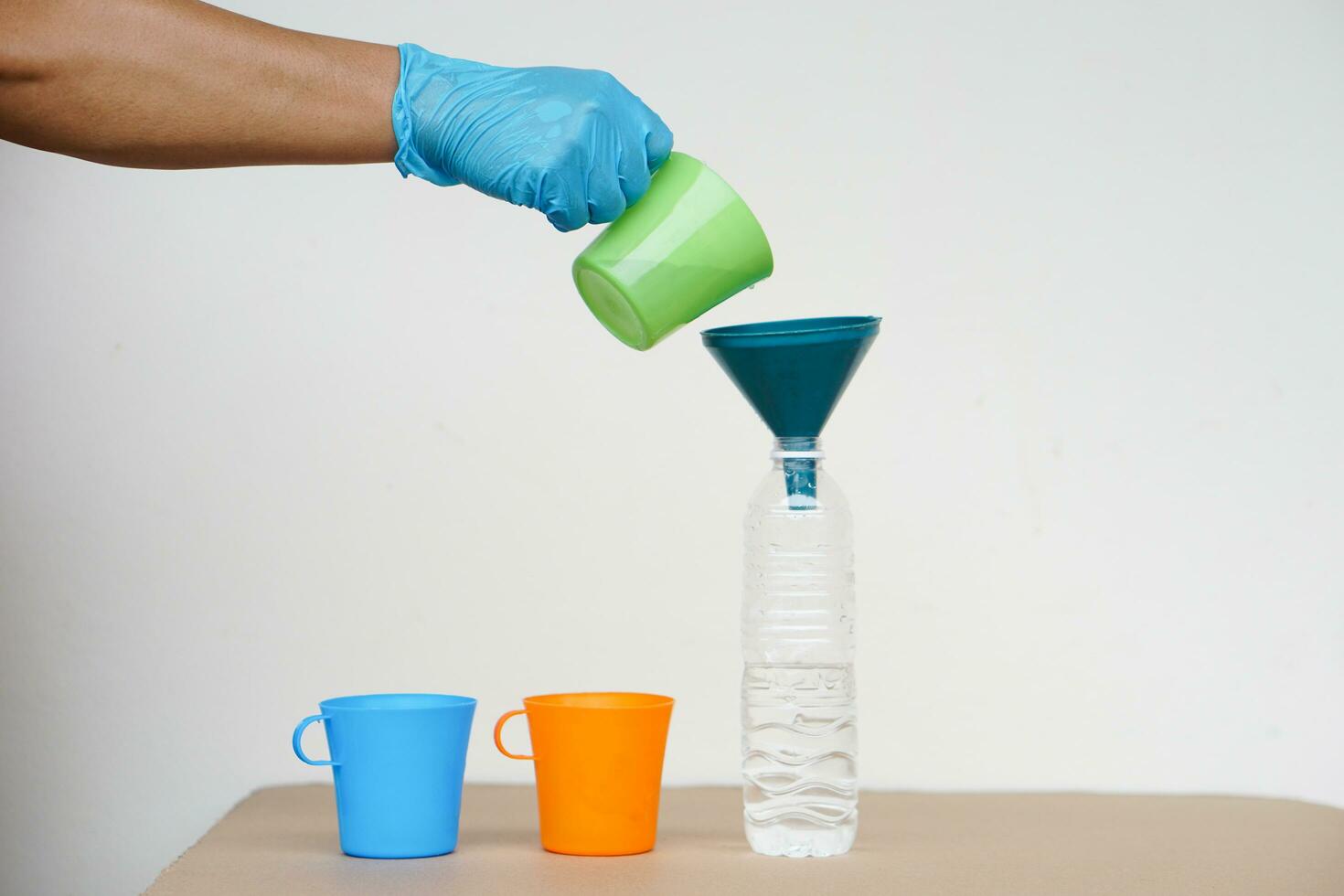 Closeup hand wear blue glove holds green mug to pour water into bottle to do science experiment. Concept, water quantity measurement  for mixing chemical substances. photo