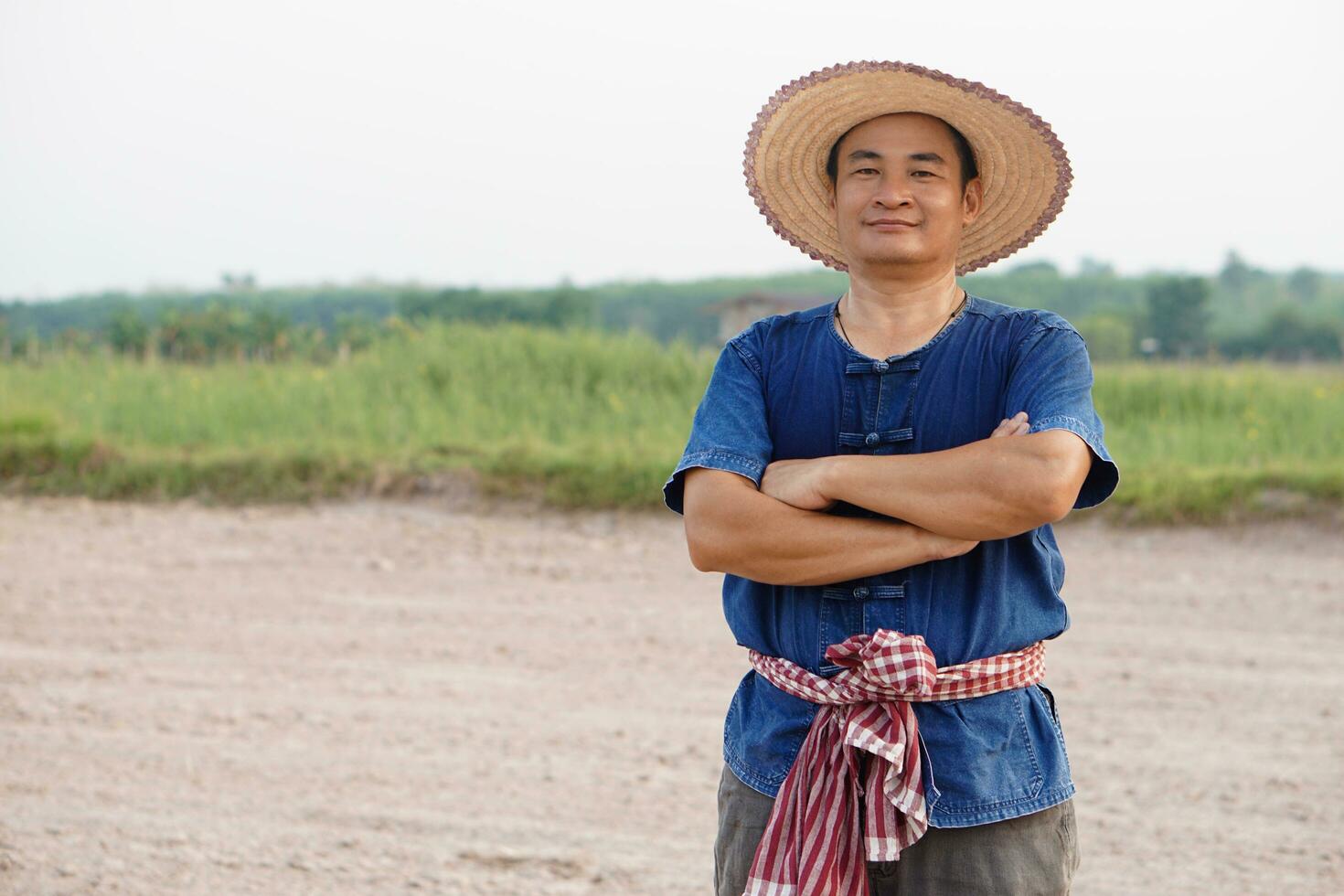 Handsome Asian man farmer wears hat, blue shirt, crossed arms on chest , feel confident.  Concept , Agriculture occupation. Thai Farmer . photo