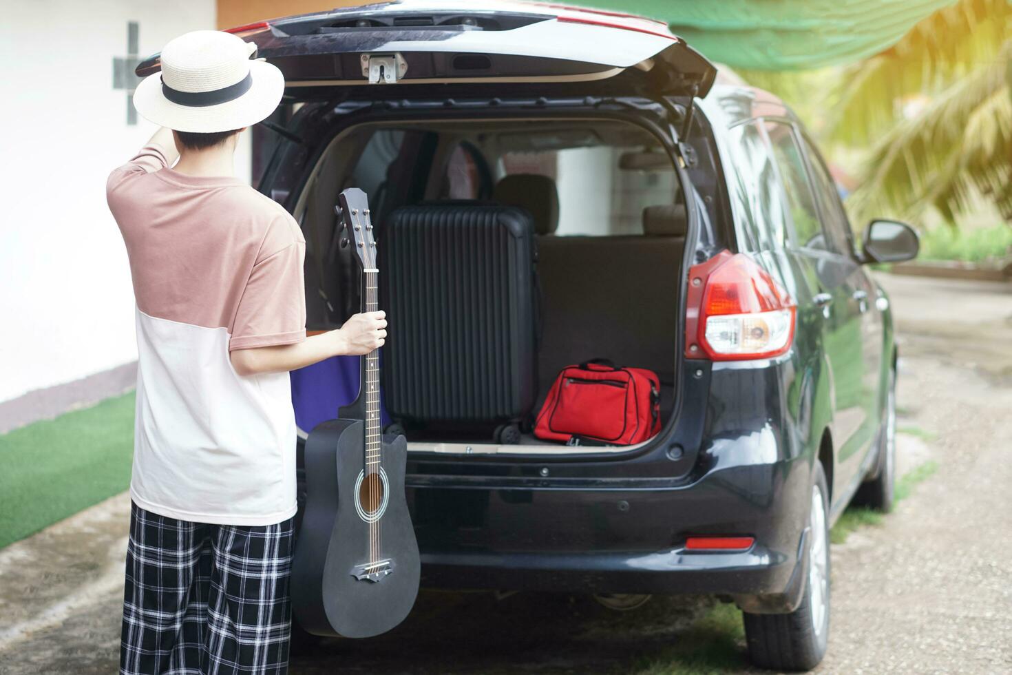 Back view of Asian man holds the guitar and take luggage into his car.Concept, travelling, going by car. Vacation, holiday or weekend trip. Prepare and ready go. photo