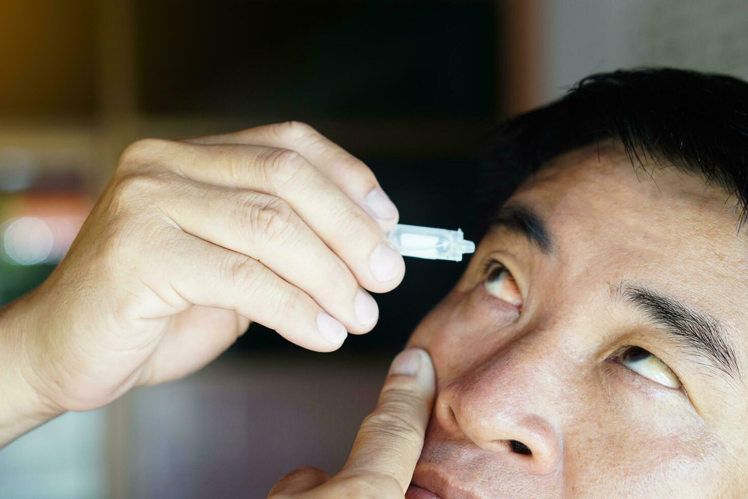 Asian man uses artificial tear lubricant eye drops with his eyes. Concept, Healthcare. Treatment for dry eye symptoms, eye inflammation diseases. Relief irritated optics. photo