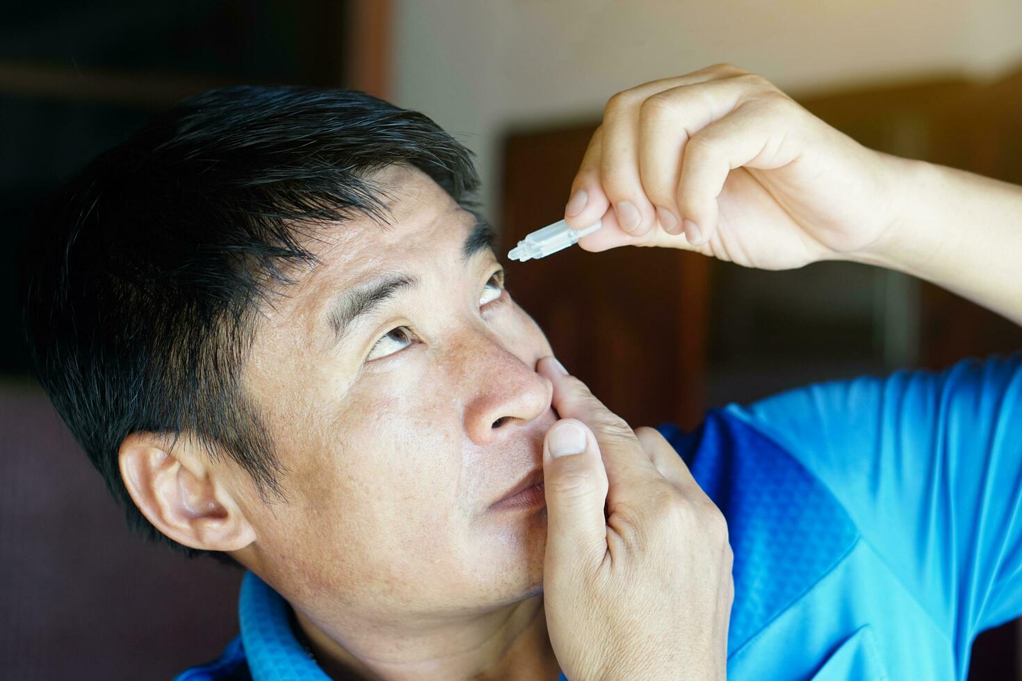 Asian man uses artificial tear lubricant eye drops with his eyes. Concept, Healthcare. Treatment for dry eye symptoms, eye inflammation diseases. Relief irritated optics. photo