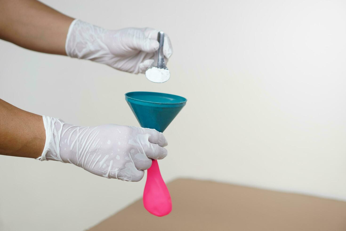 Closeup hands wears gloves holds funnel and flat pink balloon, put spoon of baking soda powder to pour into balloon. Concept, science experiment. photo