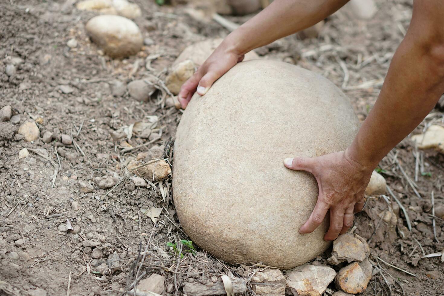 Close up hand is lifting big stone from ground. Concept, heavy. Hard working. Strong body to lift or move heavy rock. photo