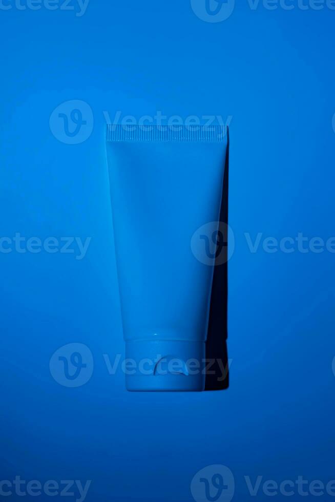 Plastic white tube on neon filter blue background. Skincare cleansing cosmetic. Beauty concept for face body care photo