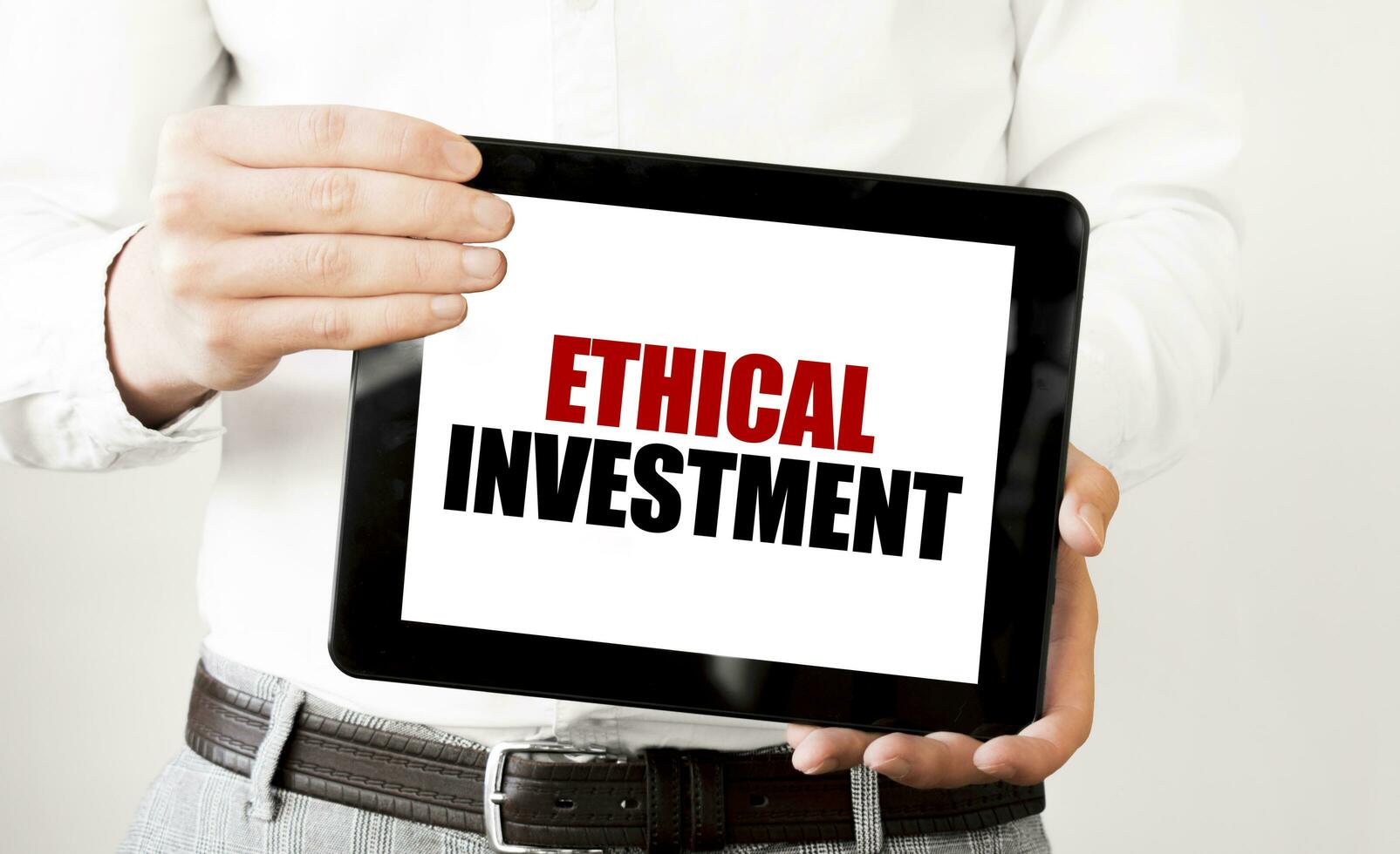 Text ETHICAL INVESTMENT on tablet display in businessman hands on the white background. Business concept photo