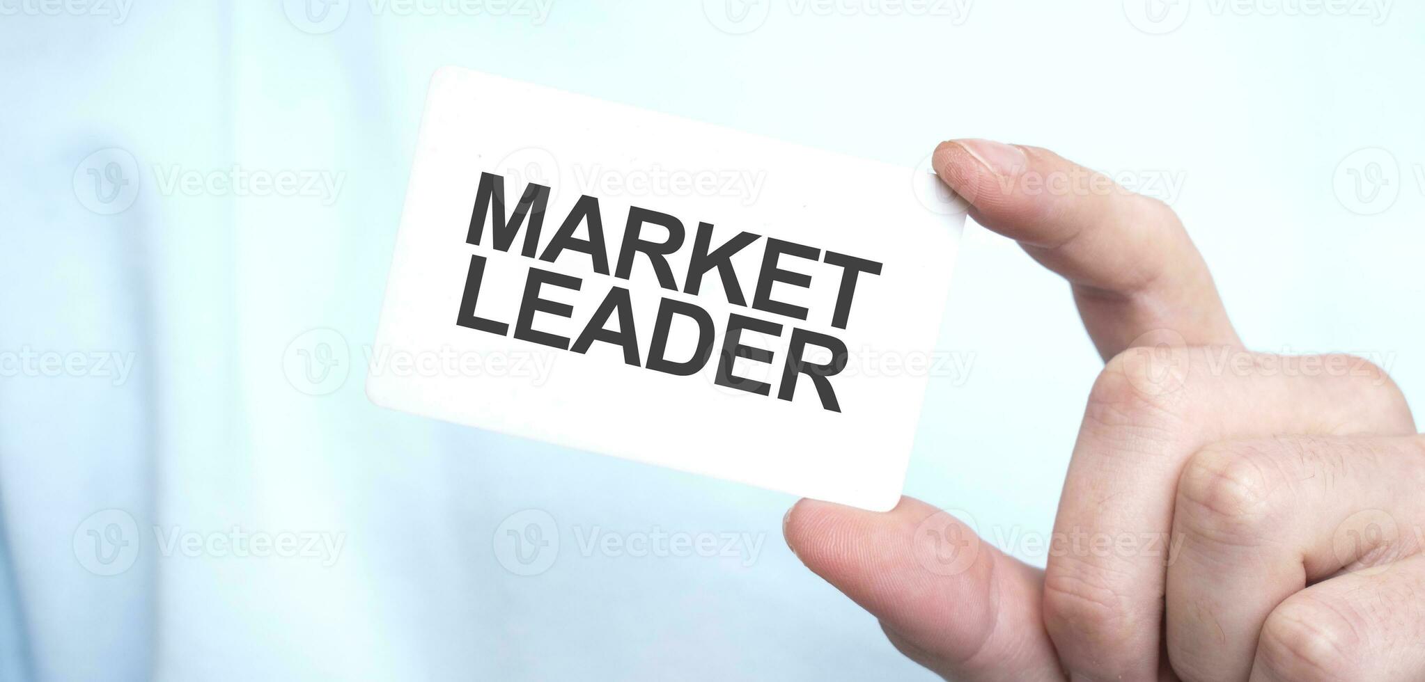 Man in blue sweatshirt holding a card with text MARKET LEADER, business concept photo