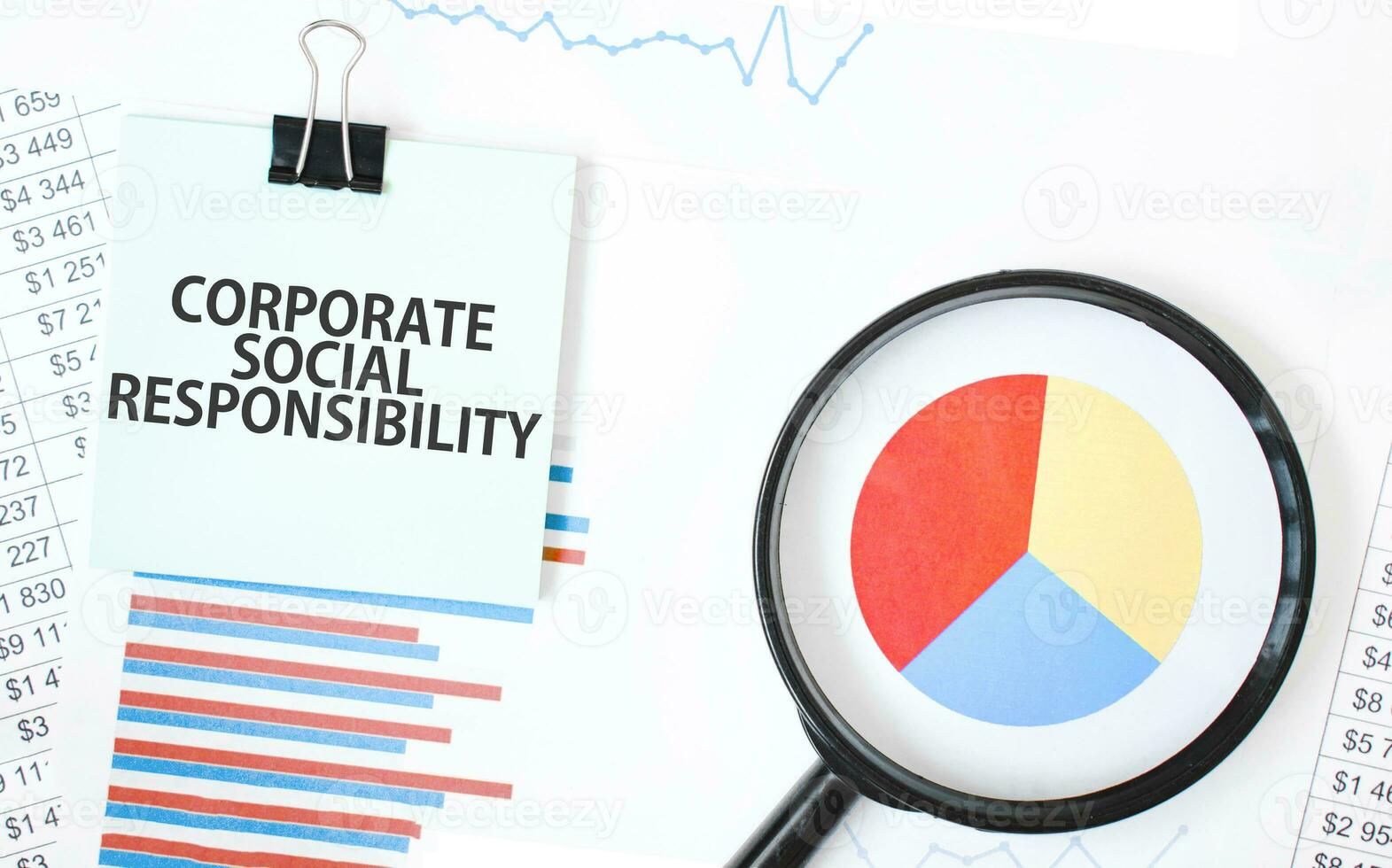 Green card on the white notepad and magnifier on the financial documentation. Text CORPORATE SOCIAL RESPONSIBILITY.. Business concept photo