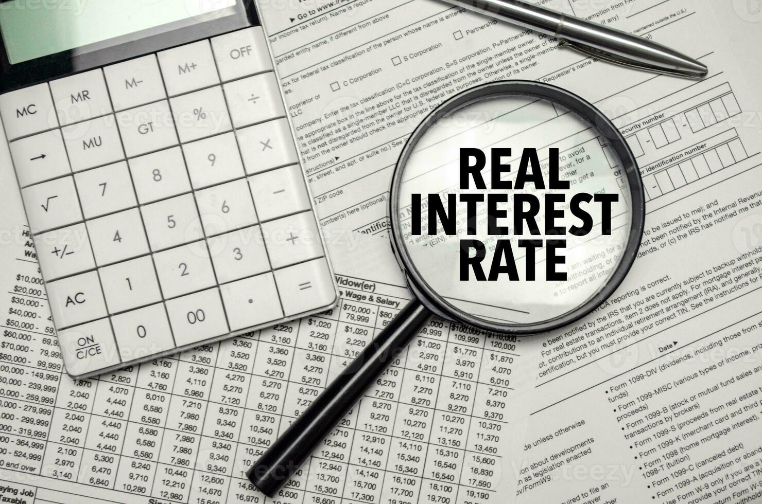 REAL INTEREST RATE words on magnifier glass and calculator with pen photo