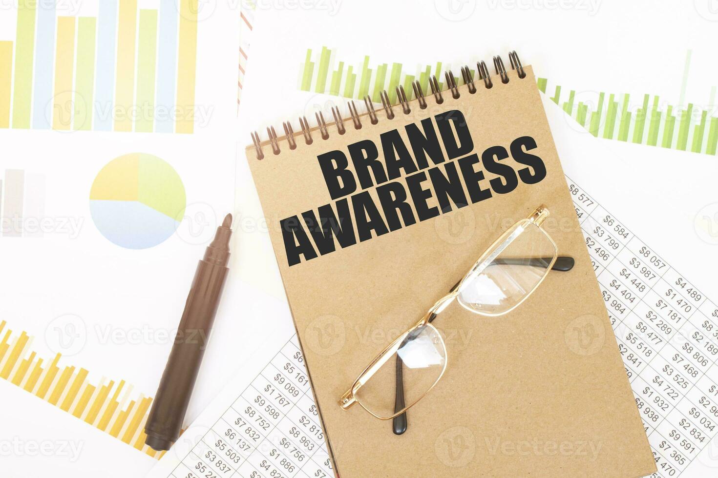In a craft colour notebook is a BRAND AWARENESS inscription, next to pencils, glasses, graphs and diagrams. photo