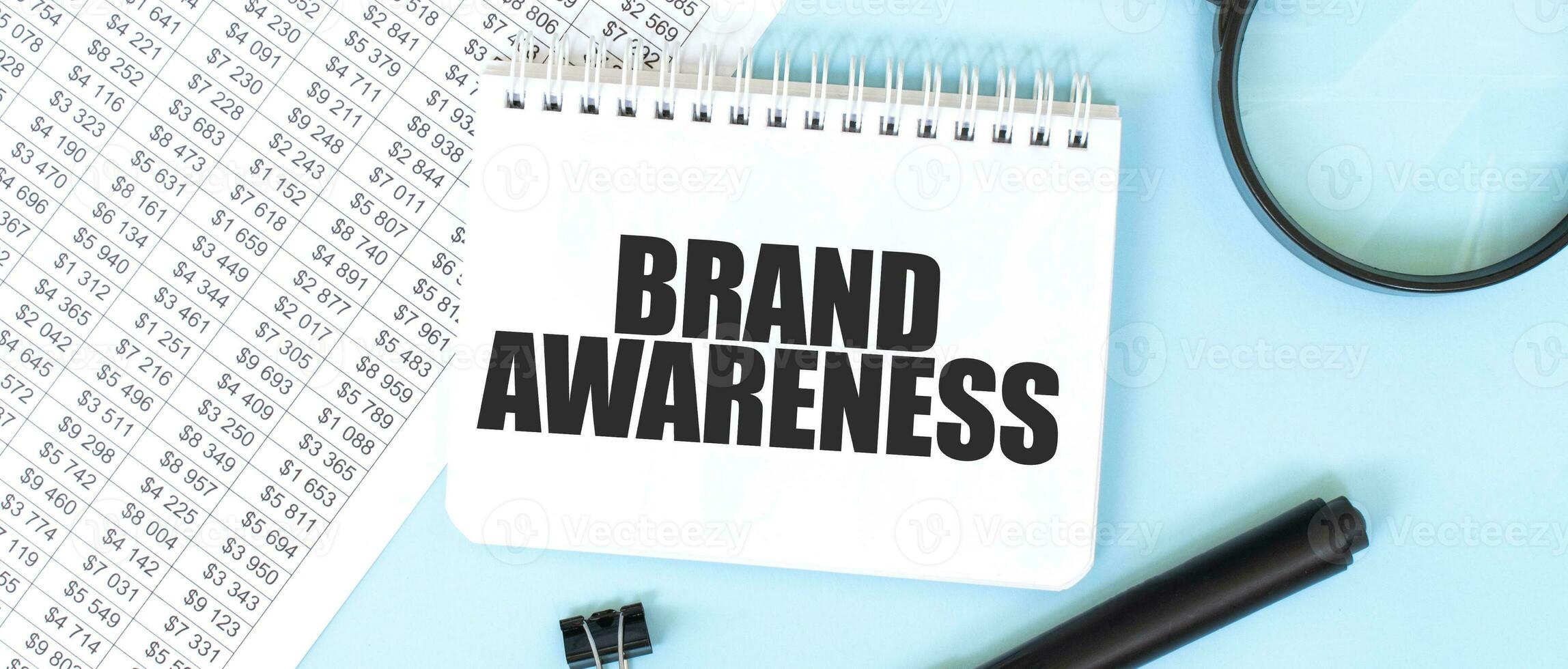 White notepad and magnifier on the financial documentation. Text BRAND AWARENESS. Business concept photo