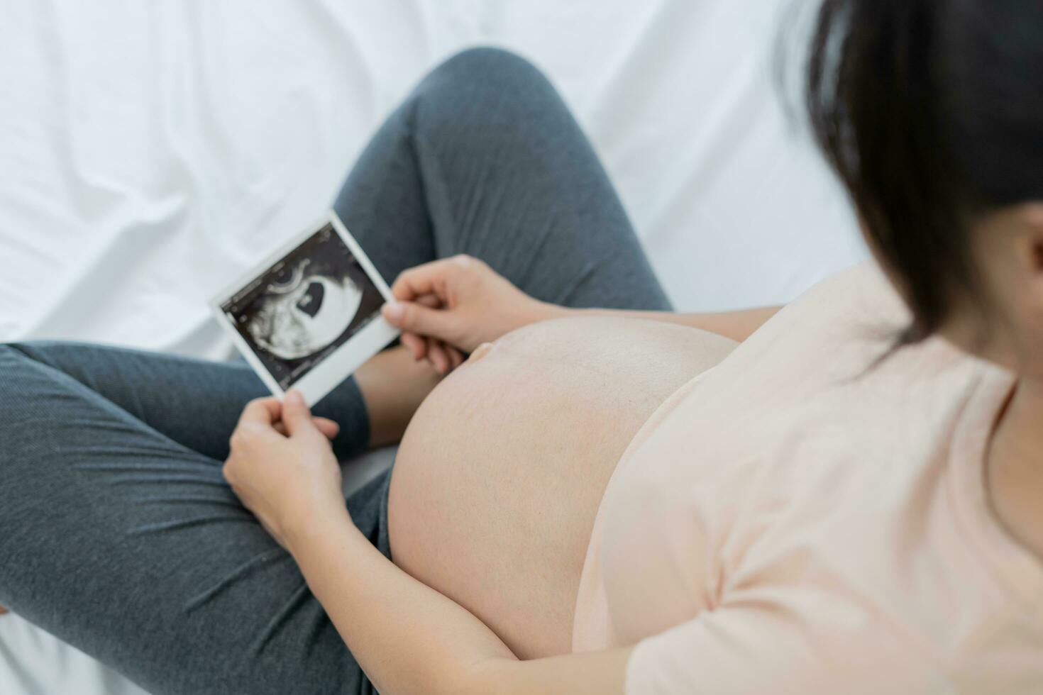 pregnant woman is looking at an ultrasound photo of fetus. Mother gently touches the baby on stomach. Happy, family, growth, pregnancy, enjoyment , prepare newborn, take care, healthcare, tummy.