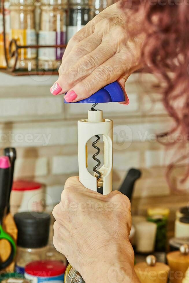 Woman opens bottle of white wine with special corkscrew photo