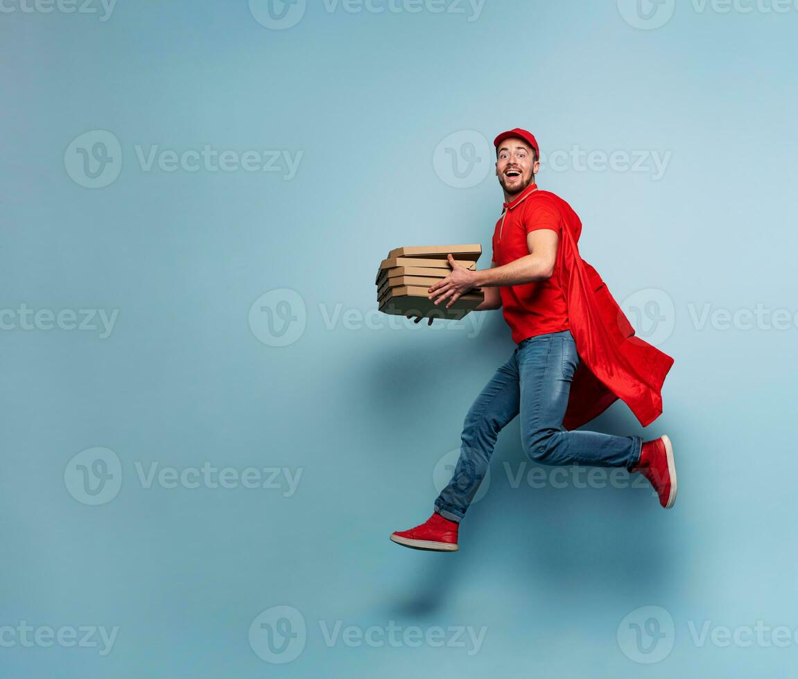 Deliveryman with pizzas acts like a powerful superhero. Concept of success and guarantee on shipment. Studio cyan background photo