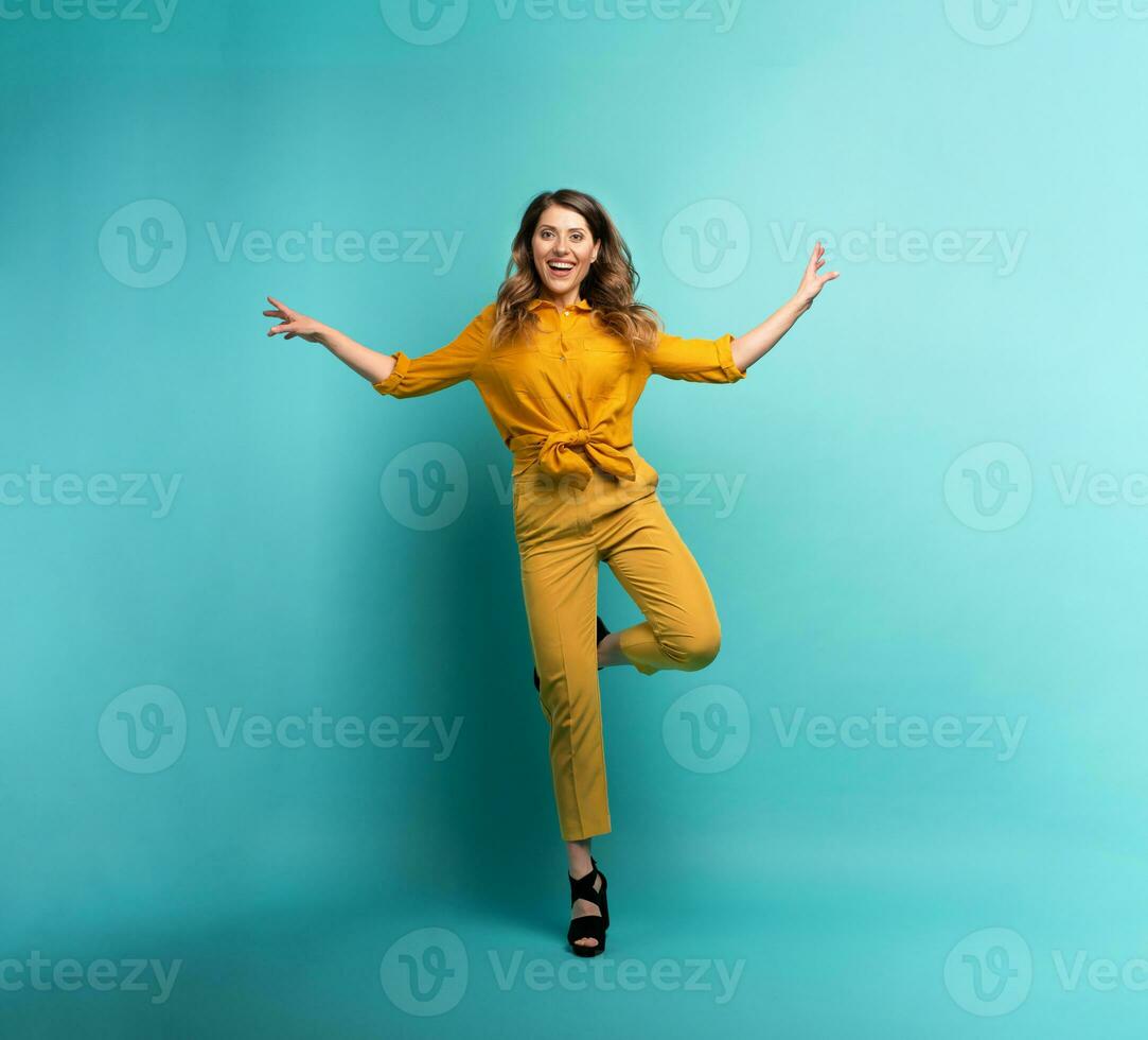 Brunette girl with a yellow clothes jumps over a cyan background. Concept of fashion and shopping with joyful expression photo