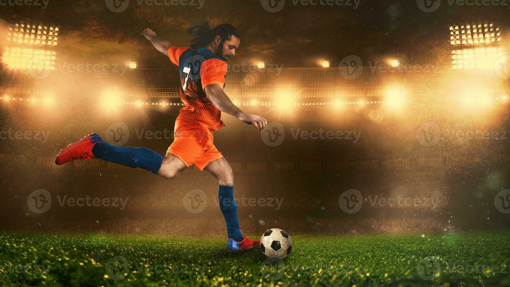 Soccer scene at night match with player in a orange uniform kicking the ball with power photo