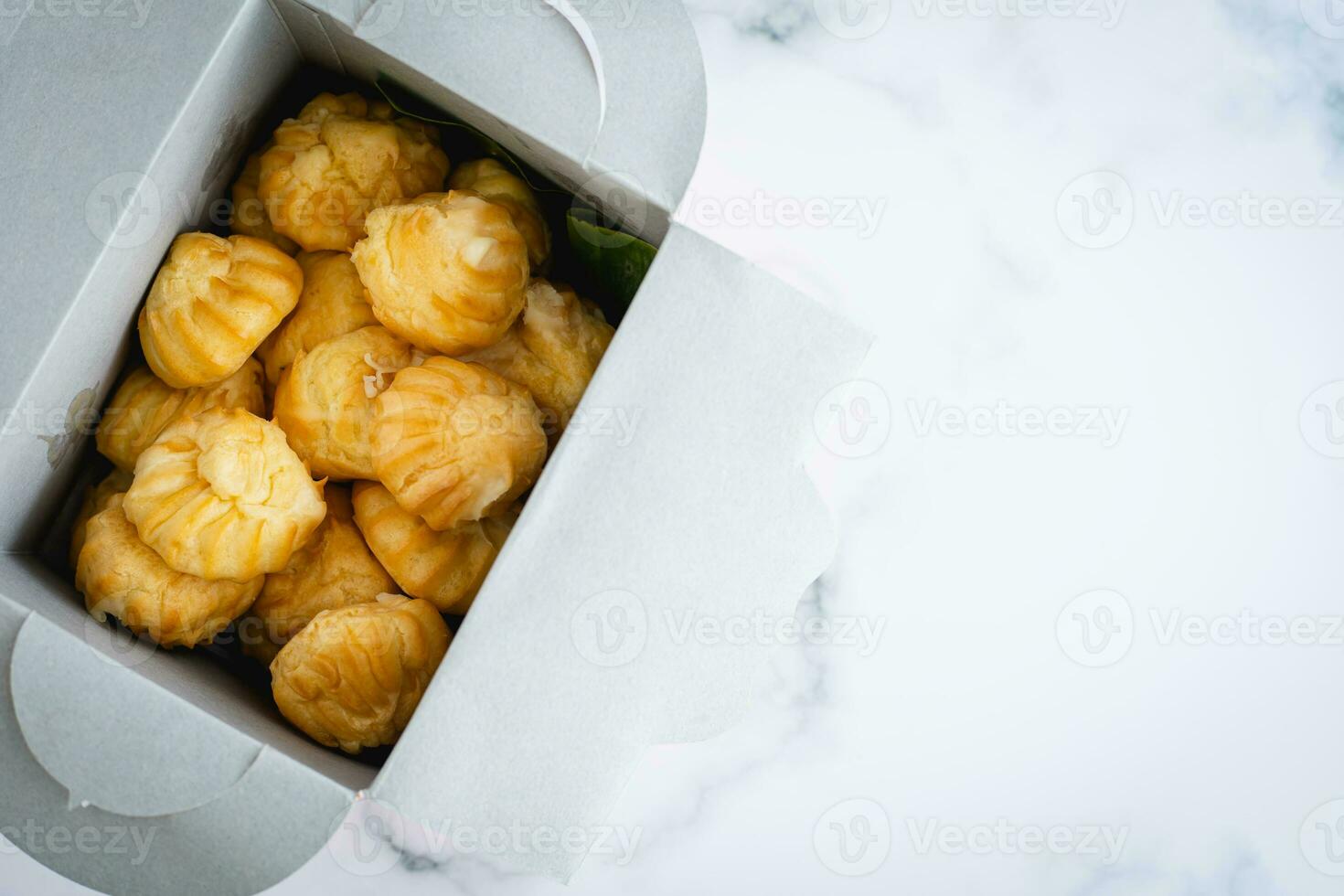 Delicious eclair vanilla cream, choux dough filled with a cream, homemade bakery in paper box packaging on white marble background photo