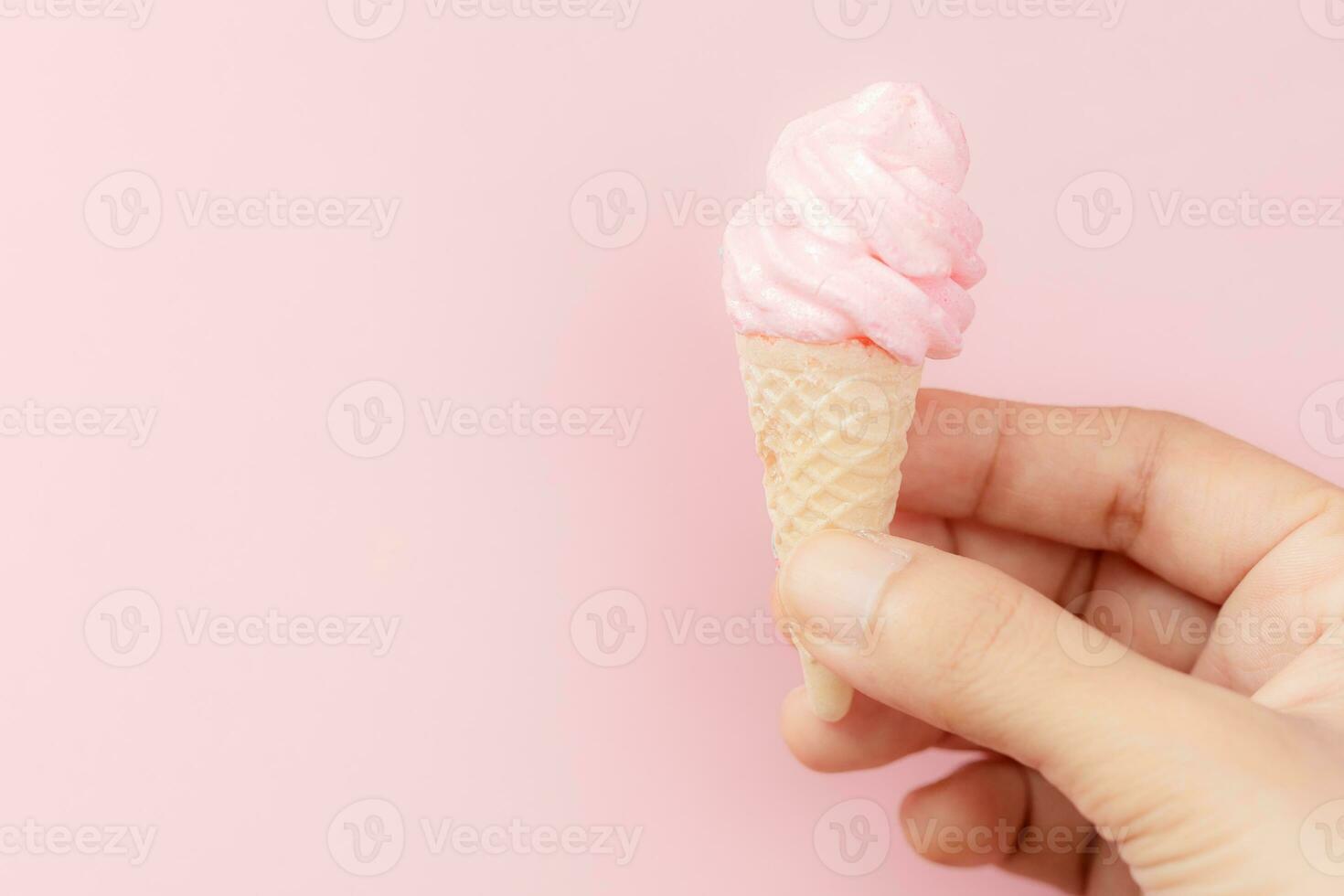 Woman's hand holding meringue ice cream cone on pink background photo